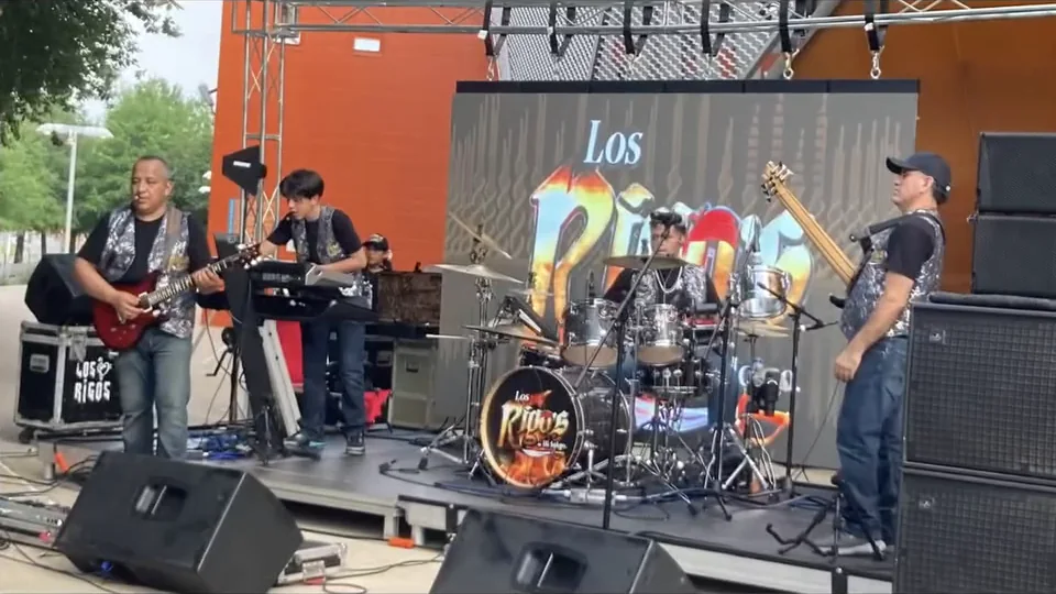 Los Rigos de Hidalgo tocando en el escenario, con su lona al fondo